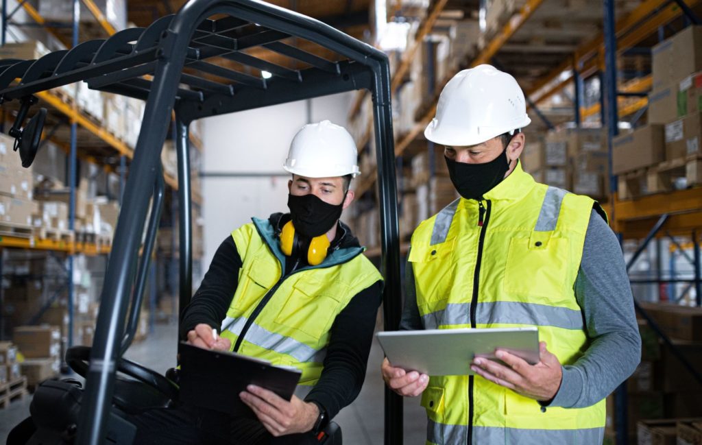 Two workers with COIVD protection meeting with tablets in warehouse 